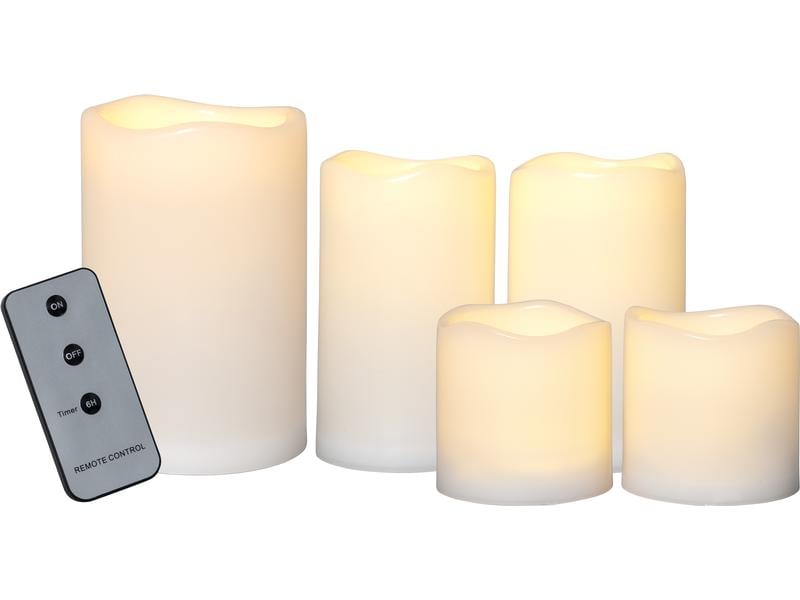Fünf beige LED-Kerzen in drei Höhen mit der zugehörigen Fernbedienung